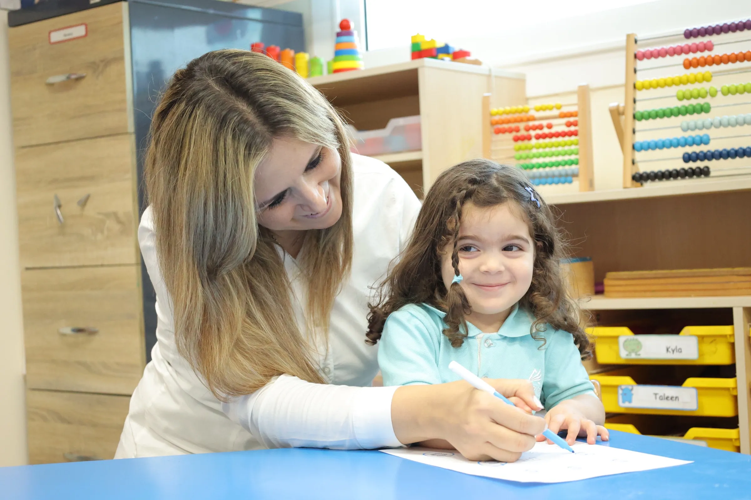 Teacher guiding a smiling young student in an Aspire EYFS classroom